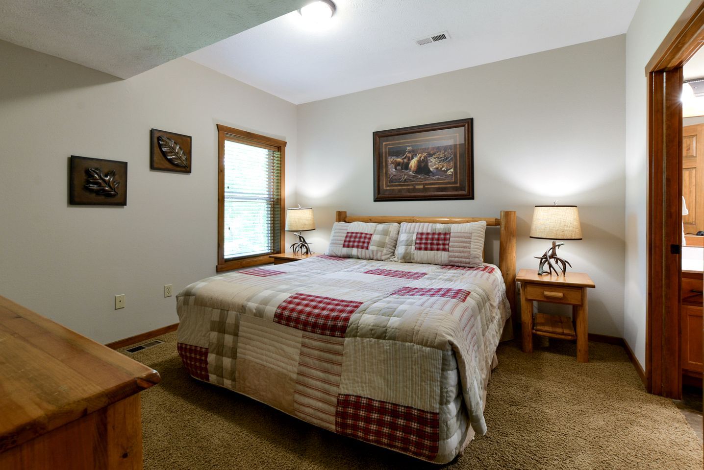 Une chambre à coucher avec un grand lit, deux tables de chevet avec des lampes, une fenêtre avec des stores et un tableau au mur.