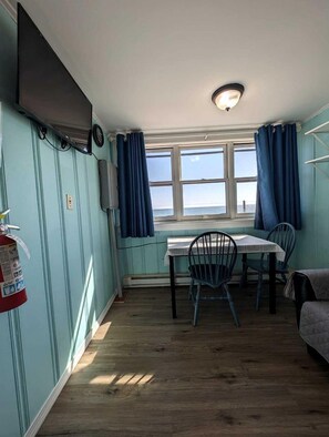A room with a table and chairs, a fire extinguisher, a television, and a window with curtains. - Private Beach Access From Your Oceanfront Cottage Stay in North Truro, Massachusetts (North Truro)