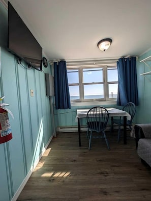 Ein Zimmer mit Tisch, Stühlen, einem Feuerlöscher, einem Fernseher und einem fenster mit Vorhängen.