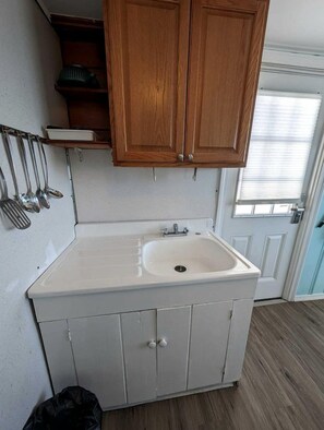 A small kitchen with white cabinets, a white sink, and wooden upper cabinets. - Private Beach Access From Your Oceanfront Cottage Stay in North Truro, Massachusetts (North Truro)