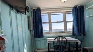 Een kamer met een tafel, stoelen, een brandblusser, een televisie en een raam met gordijnen.