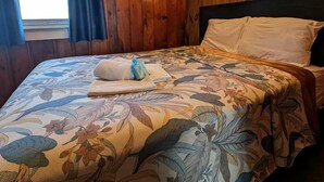 Een kamer met houten paneelwanden, een bed met bloemenbeddels, een raam met gordijnen en een wandlamp.