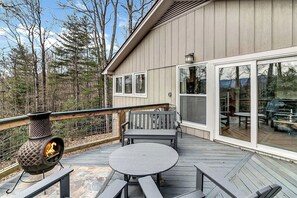 Eine Terrasse mit Kamin aus Stein, Sitzgelegenheiten und Blick auf den umliegenden Wald.