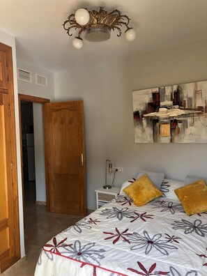 Ein Schlafzimmer mit einem Bett, einem Nachttisch, einem an der Wand hängenden abstrakten Gemälde und einer Holztür.