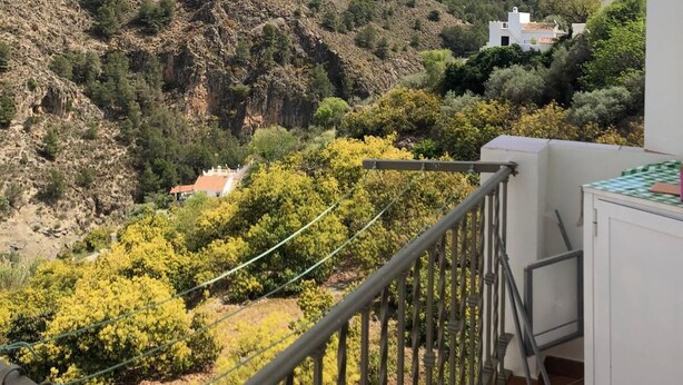 Un balcón con vistas a un paisaje montañoso, un edificio blanco y un cielo despejado.