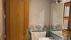 Un baño con puerta de madera, un lavabo, un espejo y un perchero para toallas.