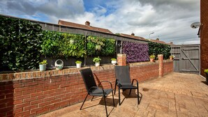 A patio with two chairs, a brick wall, and a variety of plants. - Oakdene (Stockton-on-Tees)
