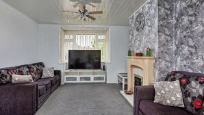 A living room with a television, sofas, a fireplace, and a ceiling fan. - Oakdene (Stockton-on-Tees)