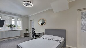 A bedroom with a bed, a desk, a chair, a round mirror, and a potted plant. - Oakdene (Stockton-on-Tees)