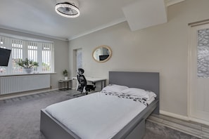 Ein Schlafzimmer mit Bett, Schreibtisch, Stuhl, einem runden Spiegel und einer Zimmerpflanze.