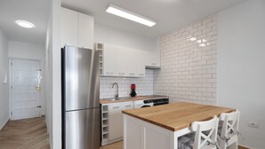 Eine moderne Küche mit weißen Schränken, einem Edelstahlkühlschrank, einer Holzinsel und einer weißen Tür.
