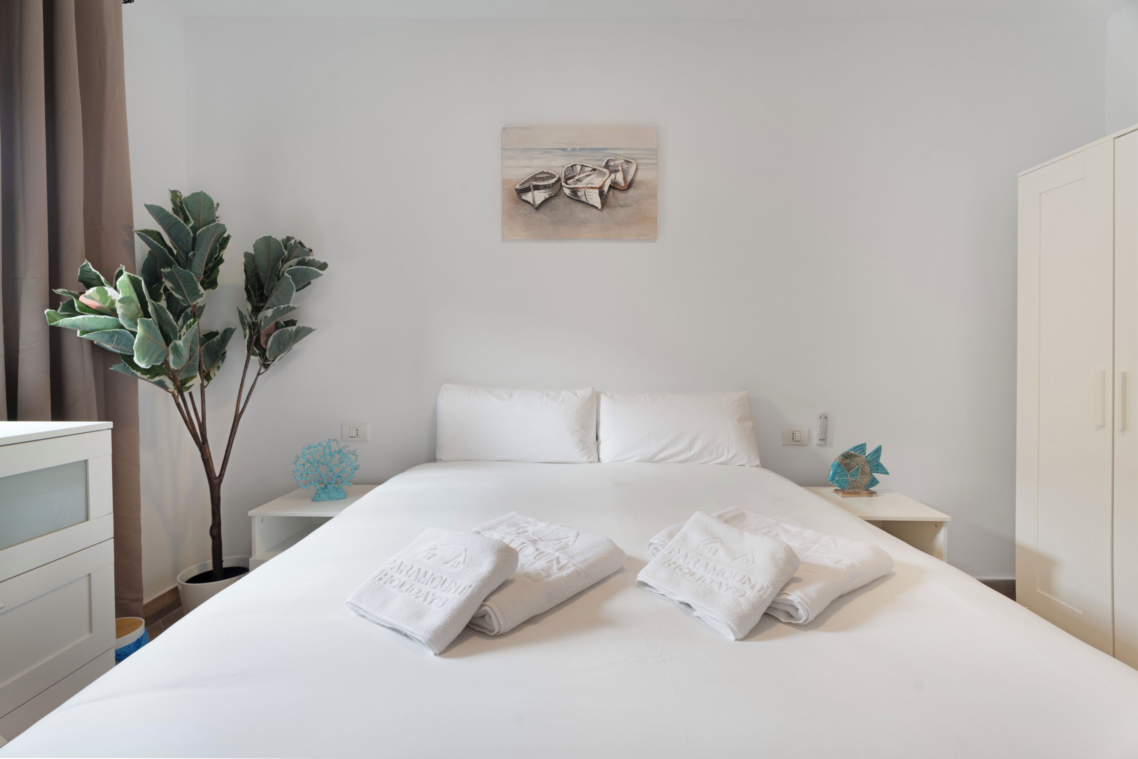 A neatly made bed with towels, a potted plant, and a wall art piece in a hotel room.