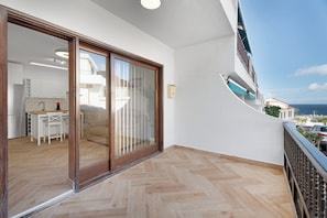 Ein Balkon mit Meerblick, eine Schiebetür zu einer Küche und ein Parkettboden mit Fischgrätenmuster.