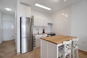 Eine moderne Küche mit weißen Schränken, einem Edelstahlkühlschrank, einem Holztisch und weißen Stühlen.