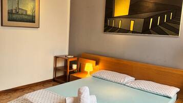 A hotel room with a bed, a bedside table, a lamp, a painting, and a view of a building.