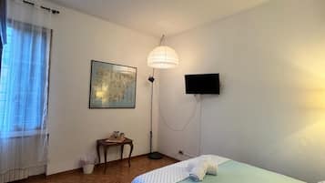 Una camera con un letto, una scrivania, una sedia, una lampada da terra e una TV a parete.