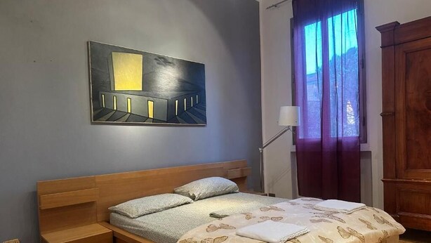 A bedroom with a bed, a nightstand, a lamp, a window with curtains, and a painting on the wall. - Bnb Fantasia (Bologna)