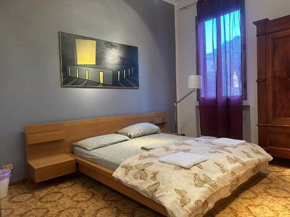 A bedroom with a bed, a nightstand, a lamp, a window with curtains, and a painting on the wall. - Bnb Fantasia (Bologna)