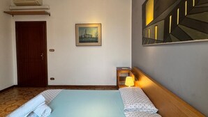 A hotel room with a bed, a nightstand, a lamp, a painting, and an air conditioning unit. - Bnb Fantasia (Bologna)