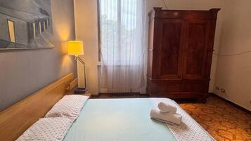 Una camera d'albergo con un letto, una testiera in legno, un comodino, una lampada, un armadio e un quadro appeso al muro.