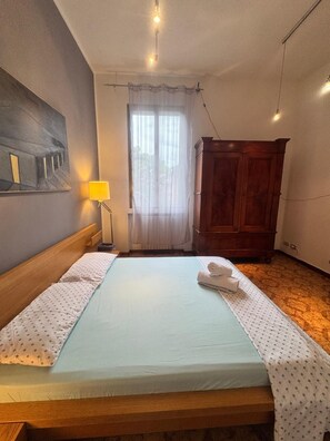 A hotel room with a bed, a wooden headboard, a nightstand, a lamp, a wardrobe, and a painting on the wall. - Bnb Fantasia (Bologna)