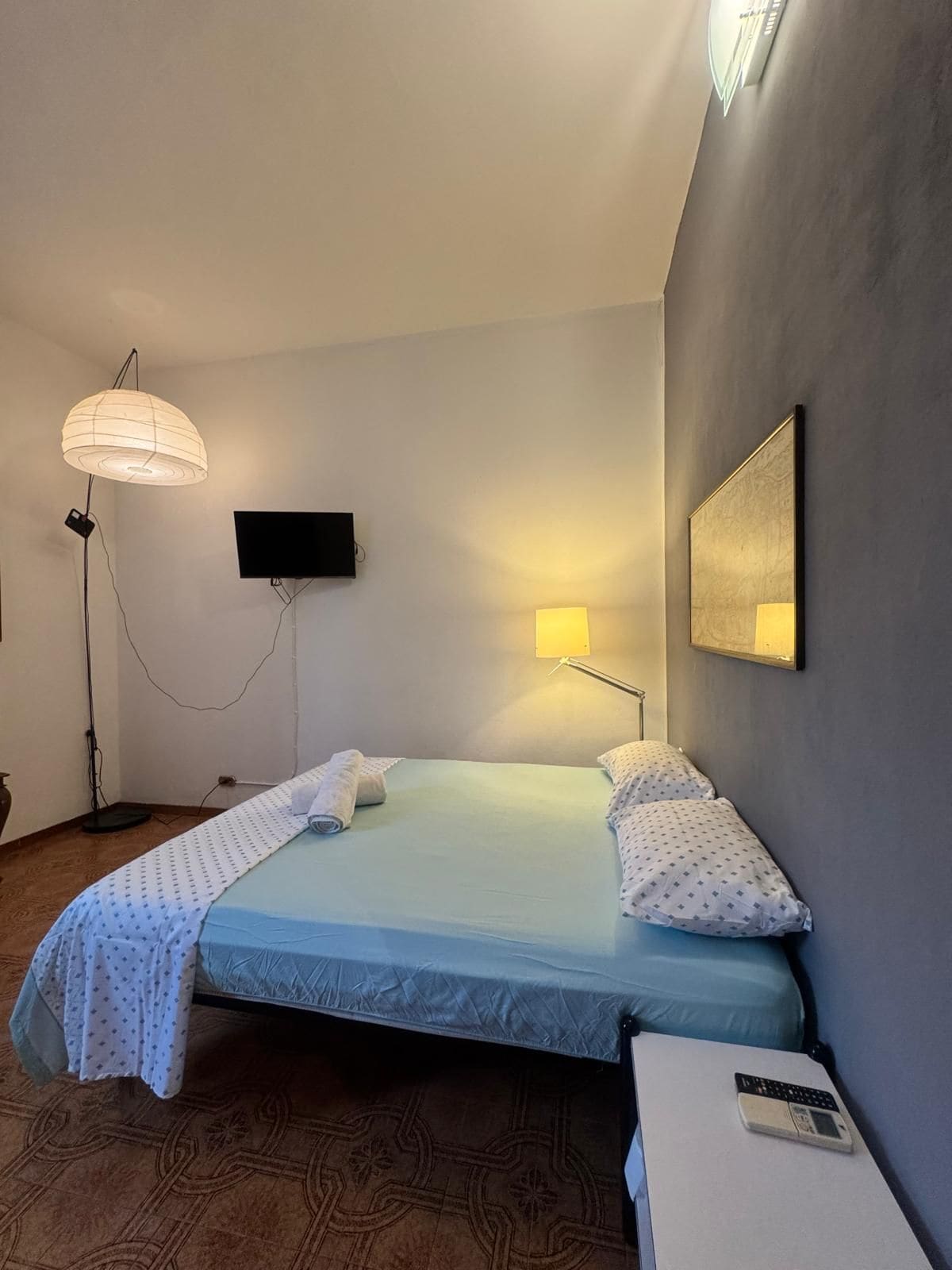 Une chambre d’hôtel comprenant un lit, une table de chevet avec un téléphone, une lampe sur pied, un téléviseur fixé au mur et un miroir mural.