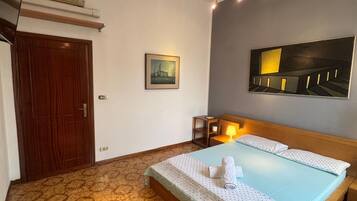 A hotel room with a bed, a small table with a tray, a painting on the wall, and a ceiling light fixture.