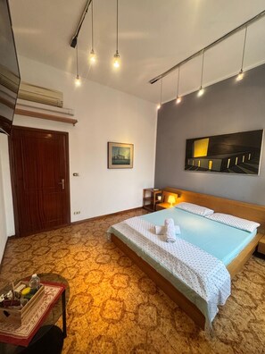 A hotel room with a bed, a small table with a tray, a painting on the wall, and a ceiling light fixture. - Bnb Fantasia (Bologna)