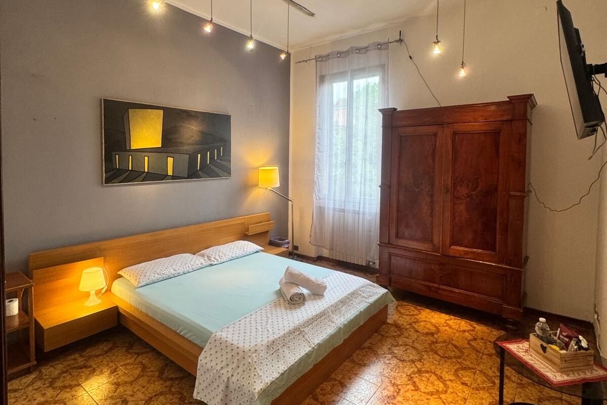 A bedroom with a bed, bedside lamps, a wooden wardrobe, and a flat-screen TV mounted on the wall.