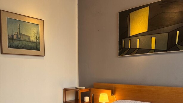 A hotel room with a bed, a nightstand, a lamp, and a painting on the wall. - Bnb Fantasia (Bologna)