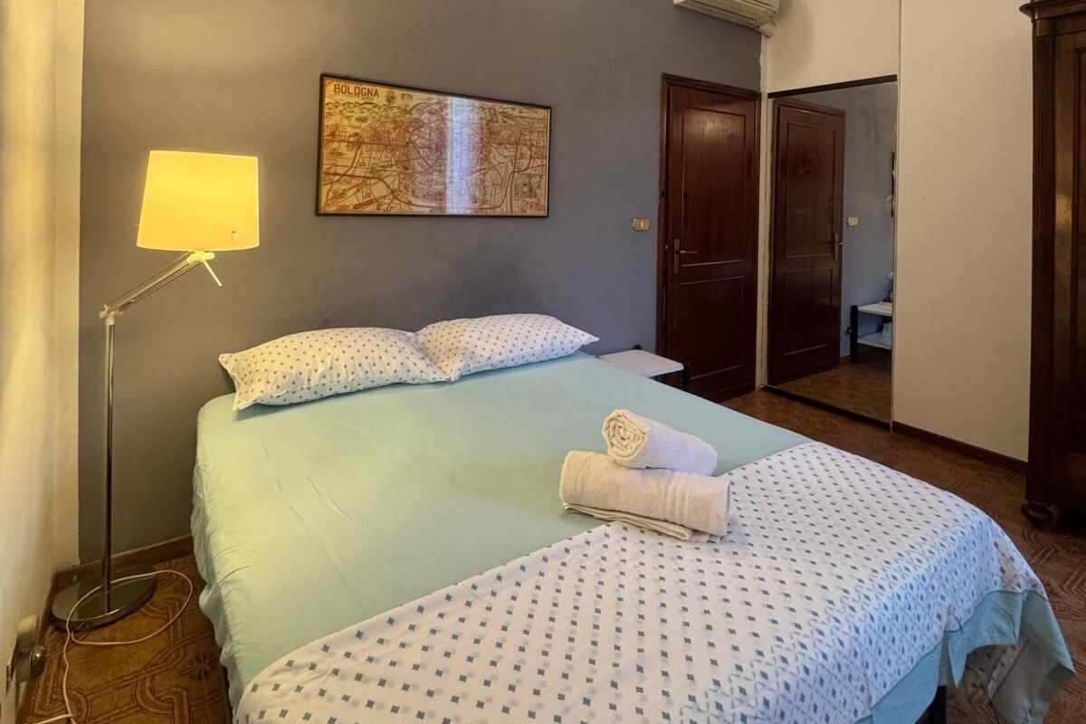 A hotel room with a bed, a map on the wall, a lamp, and a door leading to a bathroom.