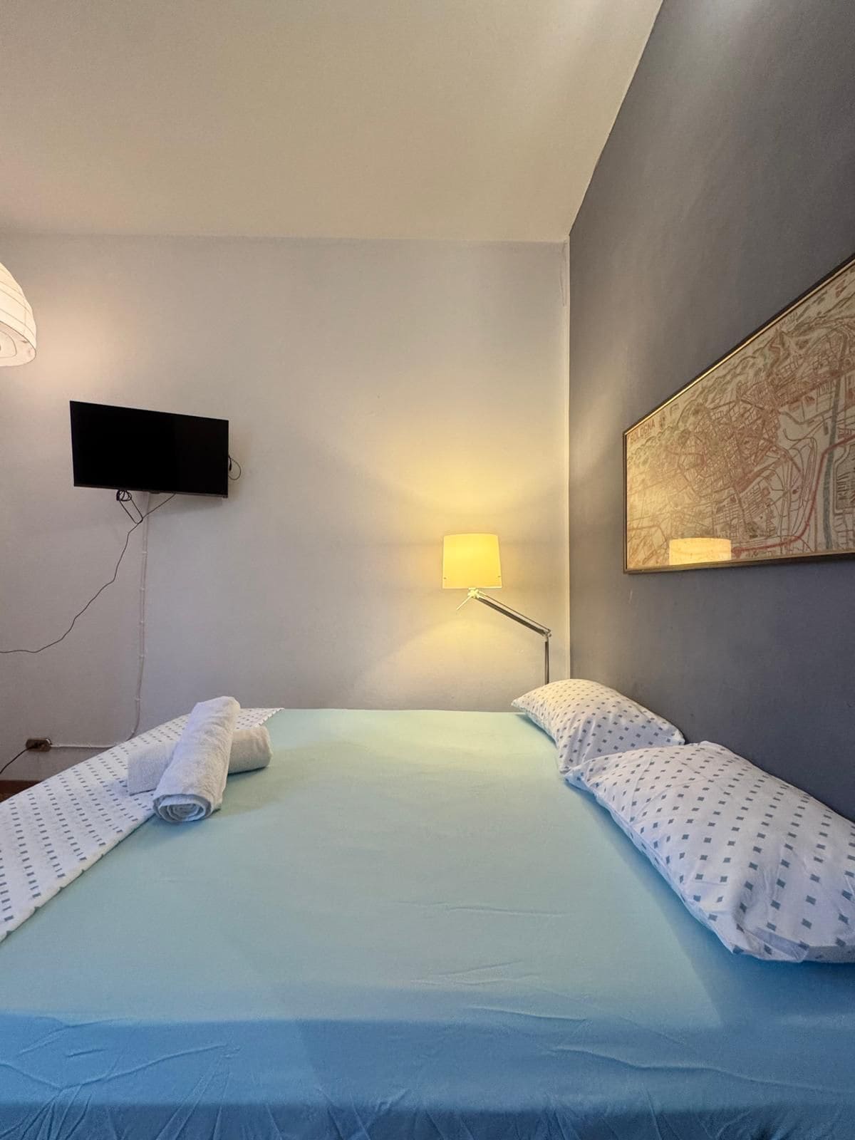 Camera d'albergo con un letto, una TV a schermo piatto fissata al muro, una lampada e una mappa incorniciata.