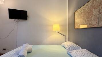 Camera d'albergo con un letto, una TV a schermo piatto fissata al muro, una lampada e una mappa incorniciata.