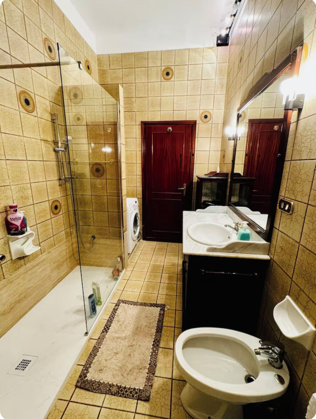 Un bagno con box doccia in vetro, lavandino, specchio e WC.
