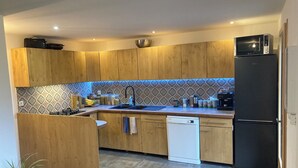 A modern kitchen with wooden cabinets, a black refrigerator, a dishwasher, and a tiled backsplash.