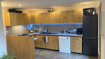 Une cuisine moderne avec des meubles en bois, un réfrigérateur noir, un lave-vaisselle et un dosseret carrelé.