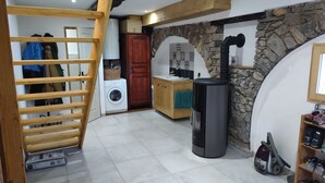 A laundry area with a washing machine, a drying rack, a wooden staircase, a stone wall, and a wood-burning stove.