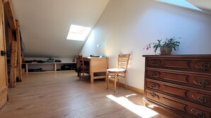 An attic bedroom with a sloped ceiling, wooden floor, a desk with a chair, a dresser, and a potted plant.