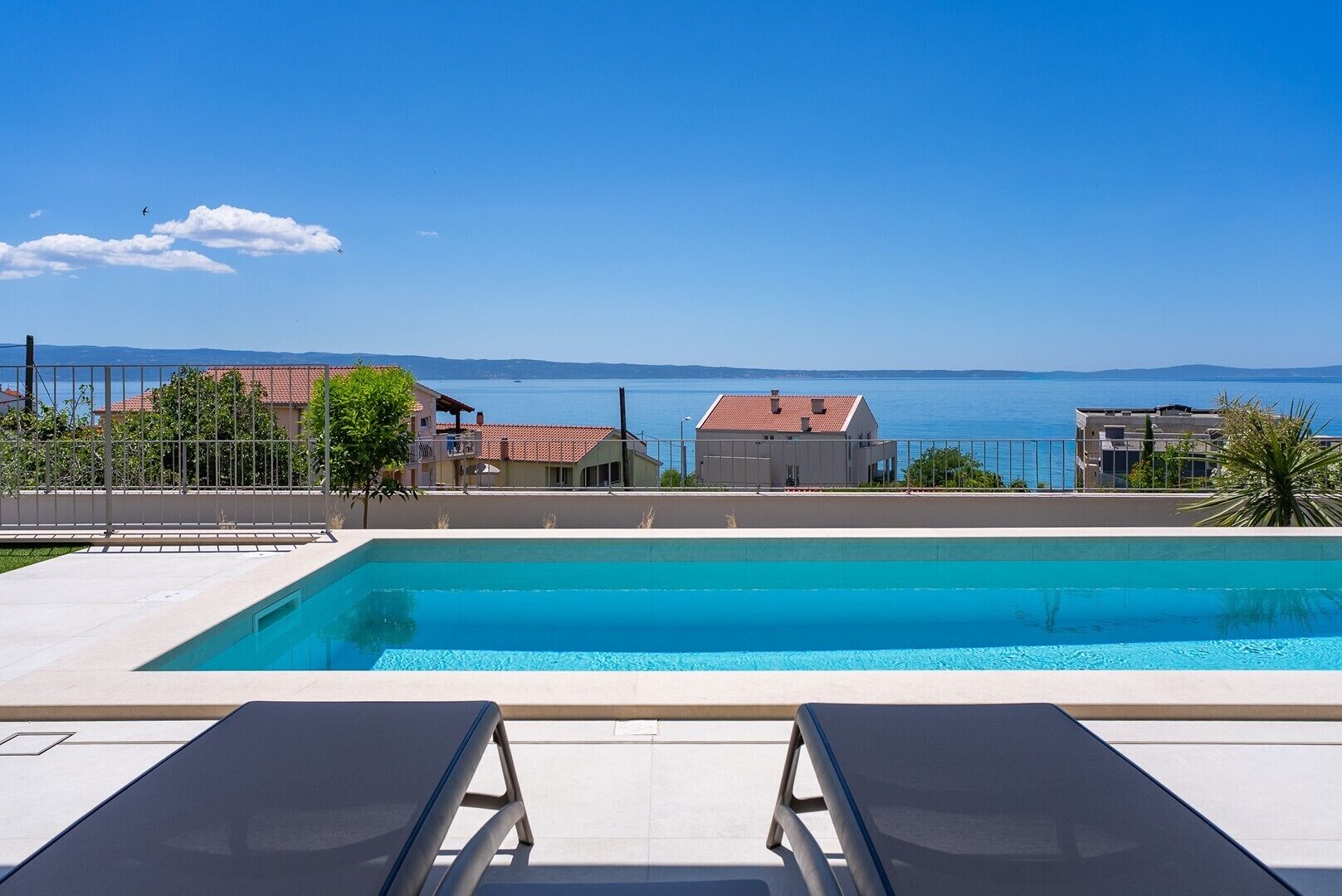 A swimming pool with lounge chairs, a view of the sea, and buildings in the background.