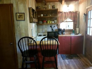 A kitchen with wooden cabinets, a stove, a microwave, and two black chairs.