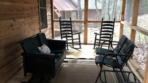 A log cabin interior with a sofa, two rocking chairs, and a rug.