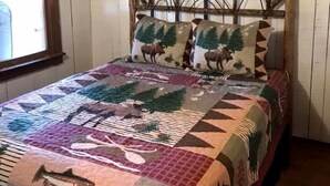 A bed with a quilt featuring wildlife and nature patterns, a wooden headboard, and a window with a curtain.
