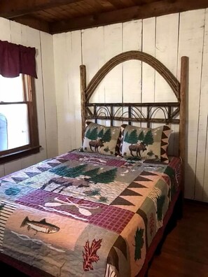Una cama con colcha adornada con motivos de fauna y naturaleza, cabecera de madera y ventana con cortina.