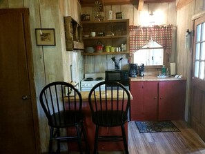 Una cocina con armarios de madera, estufa, microondas y dos sillas negras.