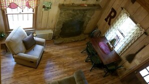 A cozy room with a stone fireplace, wooden walls, a dining table with chairs, and a sofa.