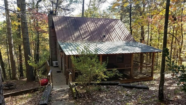 Un chalet rustique avec un toit en métal, entouré d’arbres et doté d’une terrasse en bois.