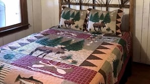 Un lit recouvert d’une courtepointe ornée de motifs représentant la faune et la nature, avec une tête de lit en bois et une fenêtre agrémentée d’un rideau.