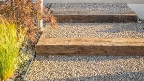 Une entrée moderne avec un escalier en bois, des plantes en pot et une vue sur l’intérieur.