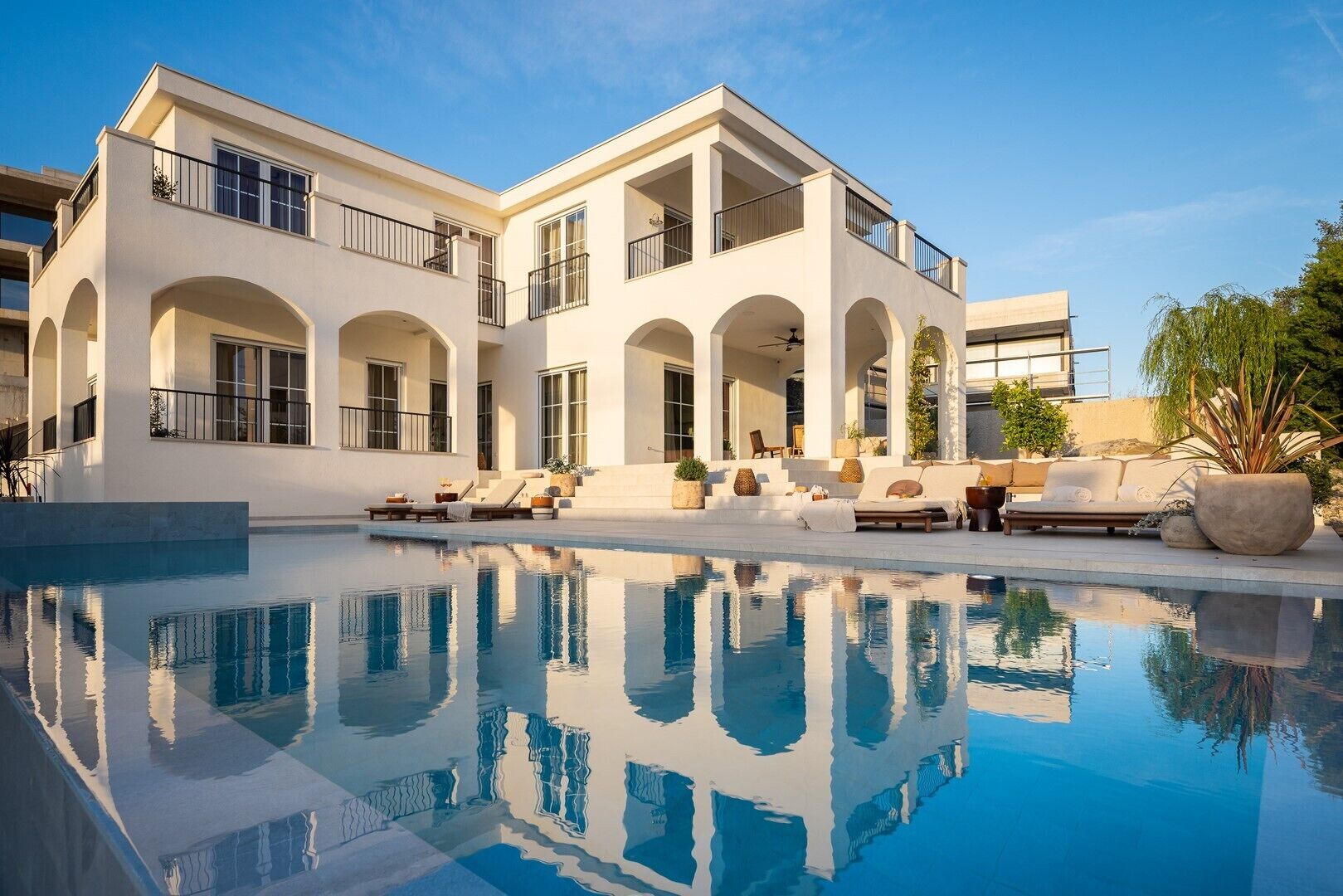 Ein modernes, zweistöckiges Haus mit Swimmingpool, Sitzgelegenheit im Freien und blauem Himmel.