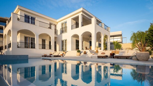 Une maison moderne à deux étages, dotée d’une piscine, d’un espace extérieur aménagé et surplombée d’un ciel d’un bleu éclatant.